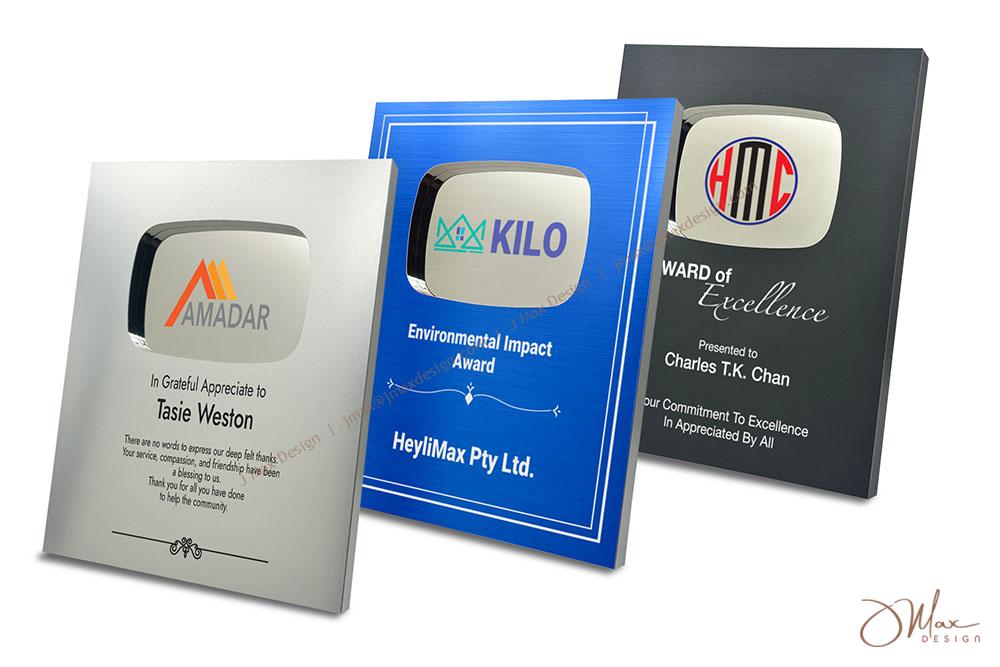 Three customizable award plaques in silver, blue, and black finishes, featuring engraved text and logos for recognition and milestone celebrations.